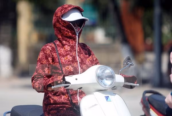 Người dân mặc kín mít để tránh nắng nóng khi ra đường. (Ảnh: Thế Duyệt/TTXVN)