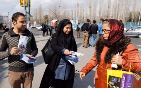 Hai người tham gia vận động tranh cử đưa phát tờ rơi cho một người dân Iran. Ảnh EPA