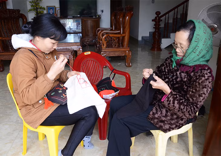 Bà Lý Thị Mai, thôn 2, xã Bằng Cả dạy con gái thêu trang phục truyền thống trước hiên nhà.