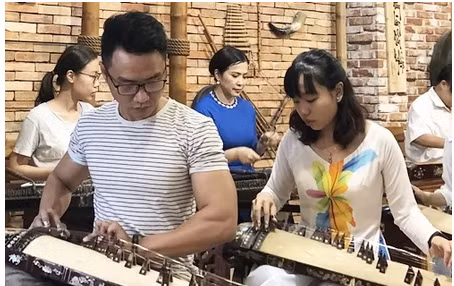 Học viên của lớp làm quen với đàn dân tộc của nghệ sĩ Tuyết Mai (áo dài xanh, hàng sau). Ảnh: Tiêu Dao.