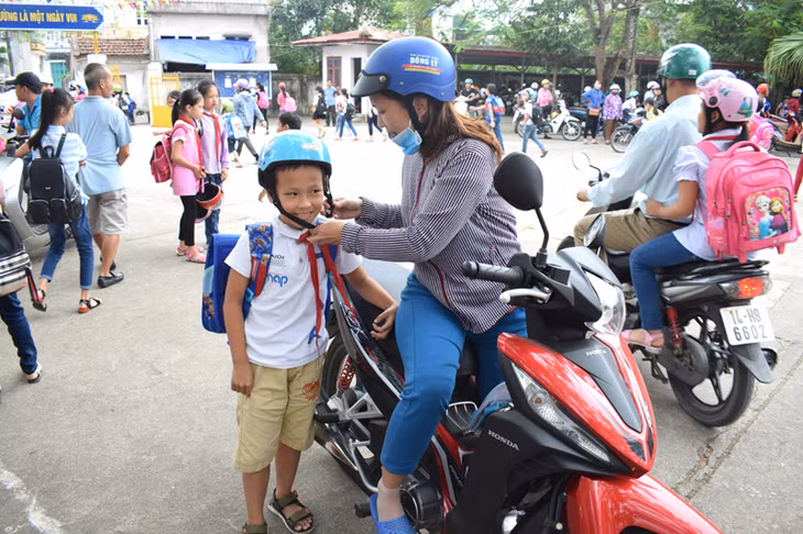 Phụ huynh học sinh trường Tiểu học thị trấn Đầm Hà nghiêm chỉnh đội mũ bảo hiểm cho con trước khi tham gia giao thông