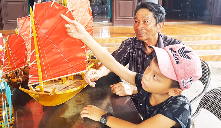 Nghệ nhân ưu tú Lê Đức Chắn chỉ cho cháu trai hình dáng chiếc thuyền buồm ba vát