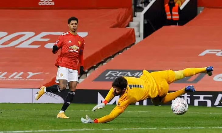 Alisson chạm tay vào bóng nhưng không thể cản cú dứt điểm của Rashford. Ảnh: Reuters.