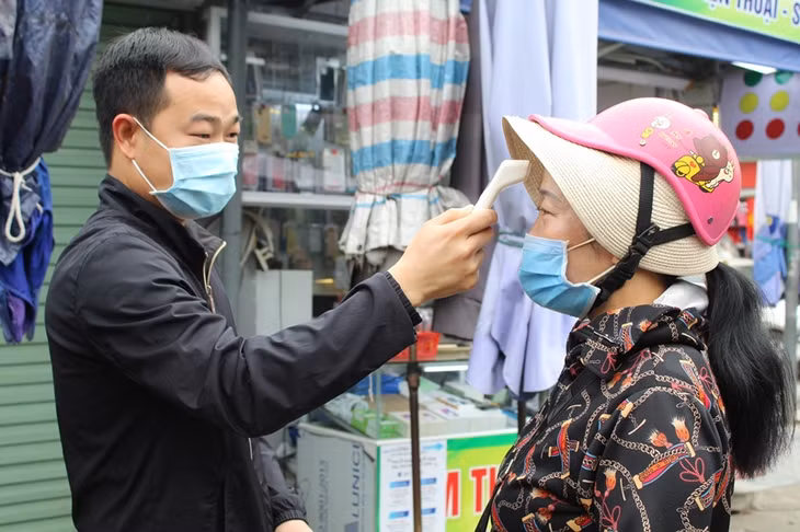 Cán bộ Ban quản lý chợ Móng Cái đo thân nhiệt cho người dân trước khi vào chợ 