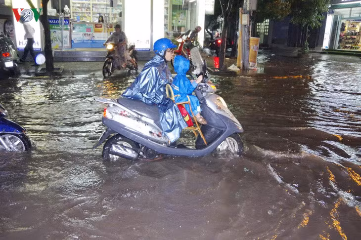  Người mẹ dắt xe chở con lội trong nước giữa cơn mưa lớn.