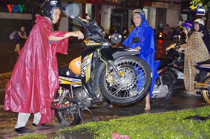 Người đàn ông cố dốc hết nước ra khỏi chiếc xe máy sau khi vượt qua một đoạn đường ngập.