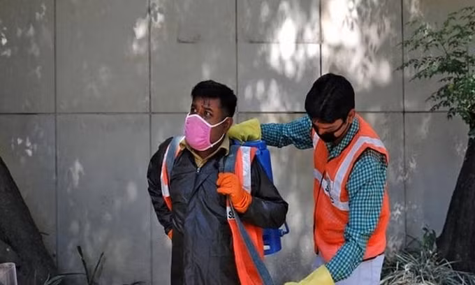 Dev Dutt Sharma (trái), được đồng nghiệp giúp đeo bình đựng dung dịch khử khuẩn lên lưng, chuẩn bị đi làm nhiệm vụ hôm 21/4. Ảnh: Reuters.