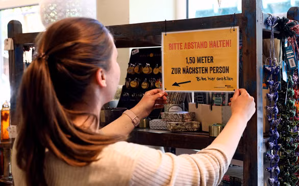 Nhân viên cửa hàng ở thủ đô Berlin (Đức) dán thông báo yêu cầu khách hàng đứng cách nhau 1,5m, ngày 18-4 - Ảnh: REUTERS