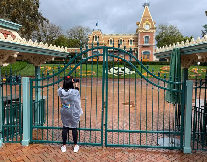 Một du khách đến Disneyland Resort ở thành phố Anaheim, California, chụp ảnh qua cánh cổng bị khóa vào 16/3. Toàn bộ Khu Disneyland Resort đã ngừng hoạt động do Covid-19. Ảnh: Jeff Gritchen/SCNG.