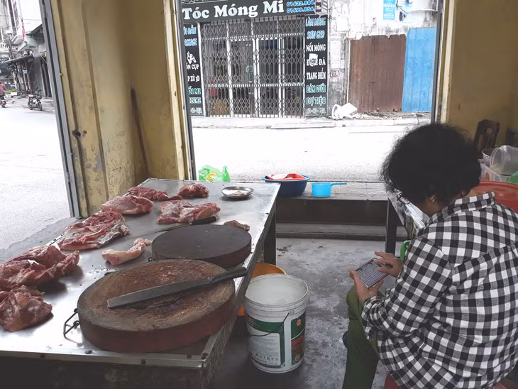Giá thịt lợn tăng, người mua dè dặt hơn, một điểm bán thịt lợn ở đường Cẩm Bình, phường Cẩm Bình, TP Cẩm Phả giải khuây bằng điện thoại thông minh