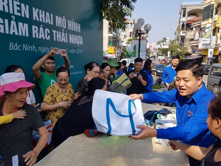 Các đoàn viên, thanh niên phát túi vải thân thiện môi trường tặng người dân và tiểu thương ở chợ Nhớn.