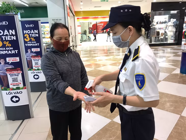 Nhân viên bảo vệ siêu thị Vinmart phun nước rửa tay khô và đo thân nhiệt cho khách hàng trước khi vào siêu thị. 