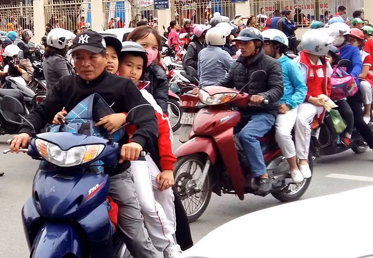 Phụ huynh chở quá số người quy định trên xe máy và cũng tuân thủ việc đội mũ bảo hiểm (Ảnh chụp tại Trường tiểu học Trần Hưng Đạo, Hạ Long)