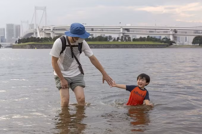 Em bé chơi đùa cùng bố trên bãi biển Odaiba ở Tokyo hôm 17/8. Ảnh: AFP