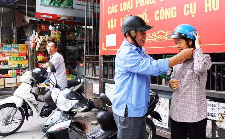 Ông Bùi Ngọc Am, thành viên Nghiệp đoàn xe ôm chợ Trung tâm hướng dẫn khách hàng đội mũ bảo hiểm đảm bảo ATGT trước khi lưu thông trên đường