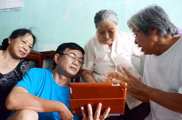 Cụ Phạm Thị Ân (thứ hai, phải sang) bùi ngùi xem những hình ảnh về ngôi mộ người con liệt sĩ.