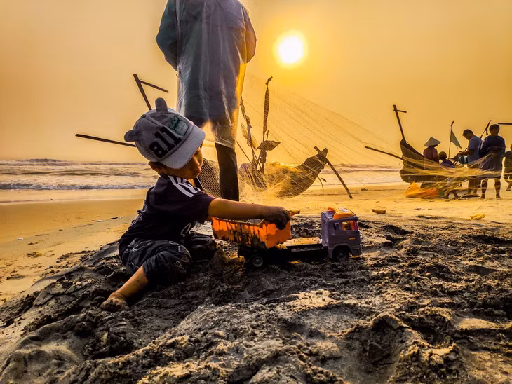 Những cậu bé chơi đùa, xây lâu đài trên cát trong khi bố mẹ gỡ lưới.