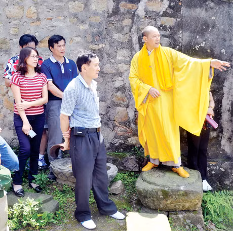 Không quản ngại nắng trưa, sư thầy nhiệt tình giới thiệu cho khách vãng cảnh về lịch sử chùa, am Ngoạ Vân. 