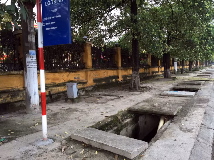 Một miệng nắp cống bị bật nắp ngay cạnh điểm đón xe buýt.
