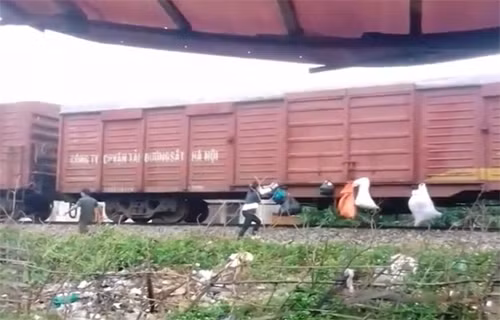 Hai người dân đang treo bao rác lên toa của tàu hàng. Ảnh: Cắt từ video.