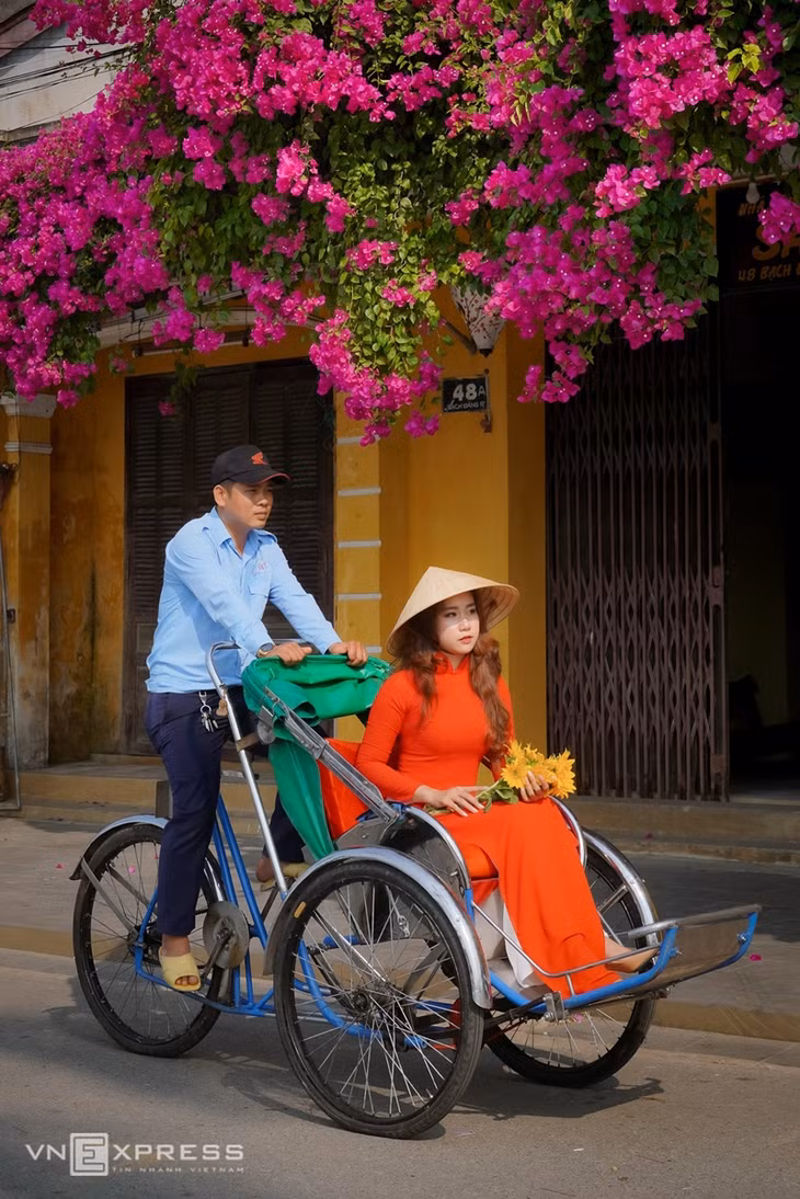 Cô gái mặc áo dài truyền thống ngồi xích lô trên đường Bạch Đằng thu hút ánh nhìn. Ven đường là hoa giấy khoe sắc làm góc phố, tường vàng như bừng sáng.
