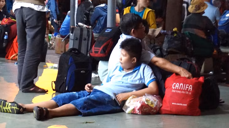 Trong ảnh, một bé trai tựa vào lưng bố, nhoài người ra sàn nhà vì mệt mỏi
