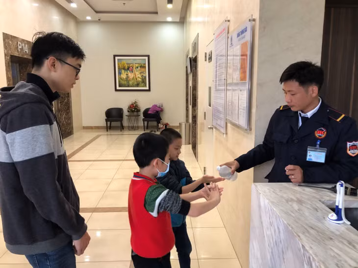 Bảo vệ Chung cư Tràng An Complex (đường Phùng Chí Kiên, quận Cầu Giấy, Hà Nội) hướng dẫn các em nhỏ sát khuẩn tay tại sảnh của tòa nhà. Ảnh: Trung Nguyên/Báo Tin tức