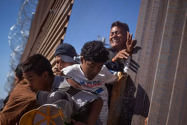 Người nhập cư cố gắng vượt tường biên giới tại Tijuana (Mexico). Ảnh: Reuters