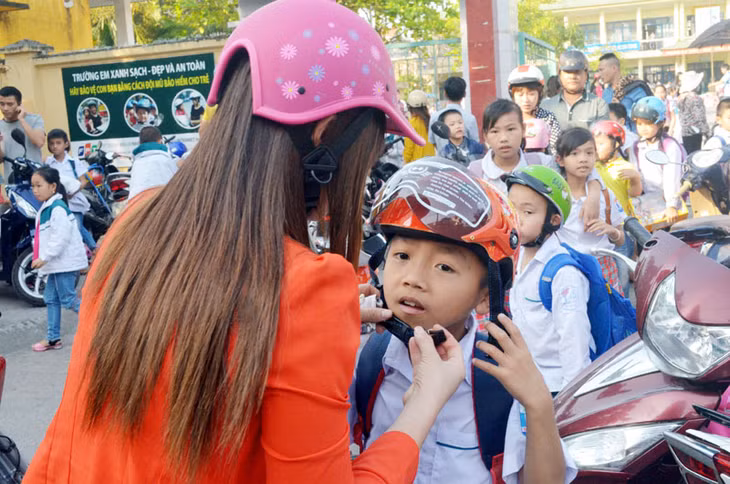 Phụ huynh đội mũ bảo hiểm cho con trước khi tham gia giao thông. (Ảnh chụp tại cổng Trường Tiểu học Đào Phúc Lộc, TP Móng Cái).