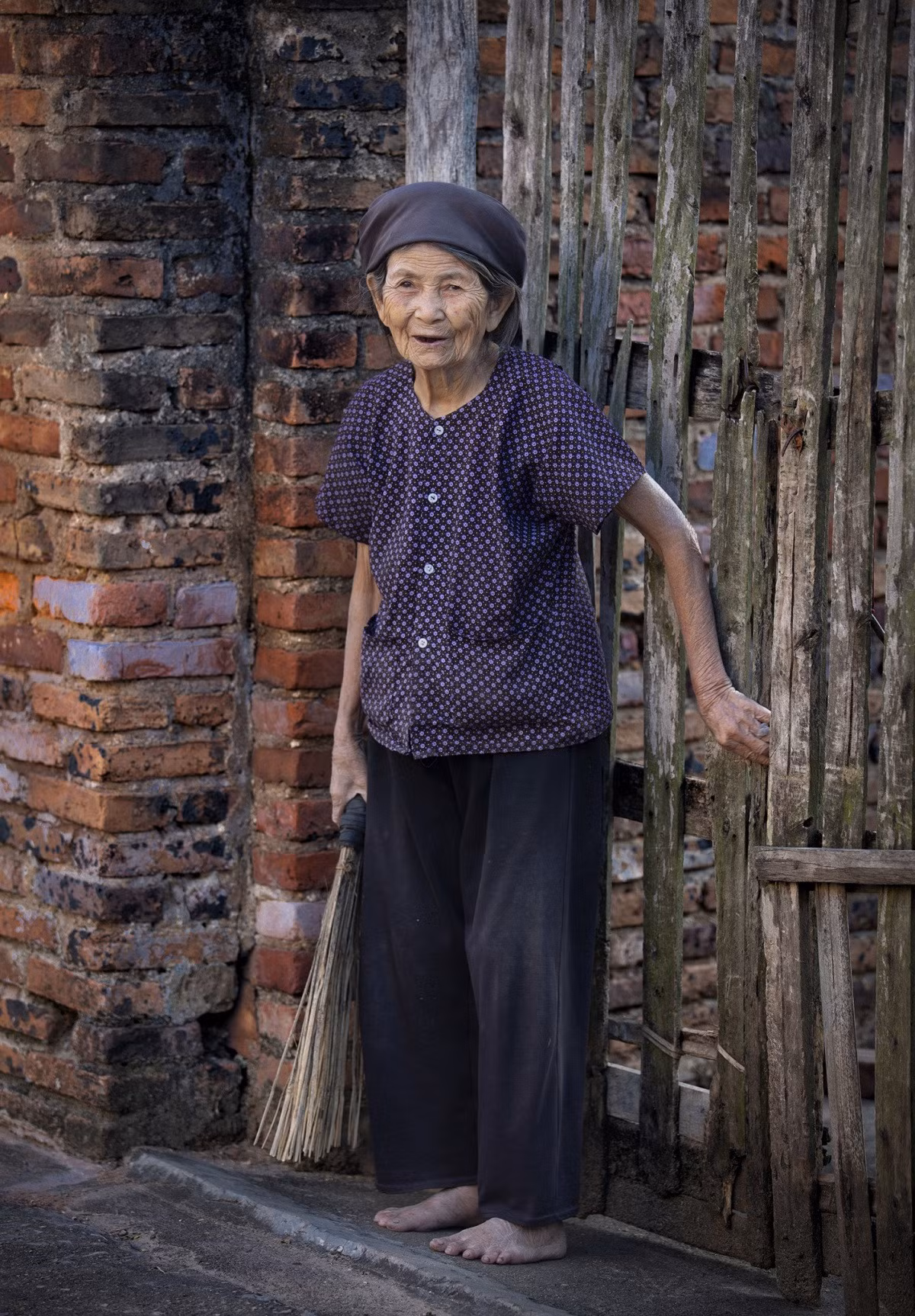 Cụ bà bên bức tường nhuốm màu thời gian, nở nụ cười, khoe hàm răng đen khi gặp ống kính. Phong tục nhuộm răng đen có từ xưa, ngày càng ít người giữ được truyền thống này.