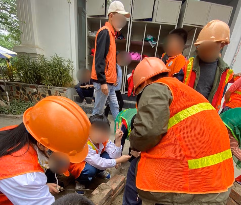 Trẻ em đang được người lớn hướng dẫn để trải nghiệm một ngày làm công nhân xây dựng. Ảnh: Đức Vân