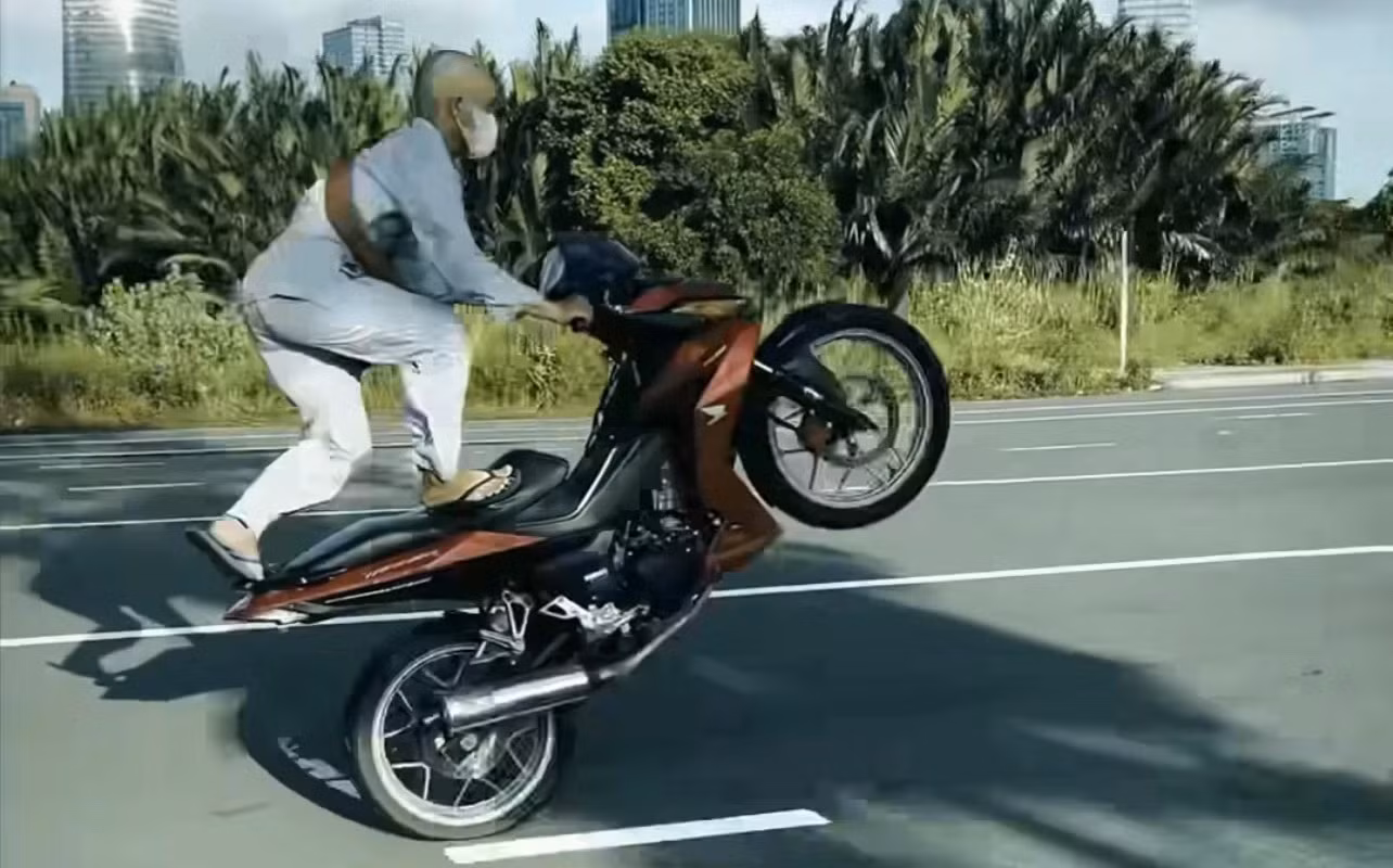 Thanh niên đứng trên yên điều khiển xe.