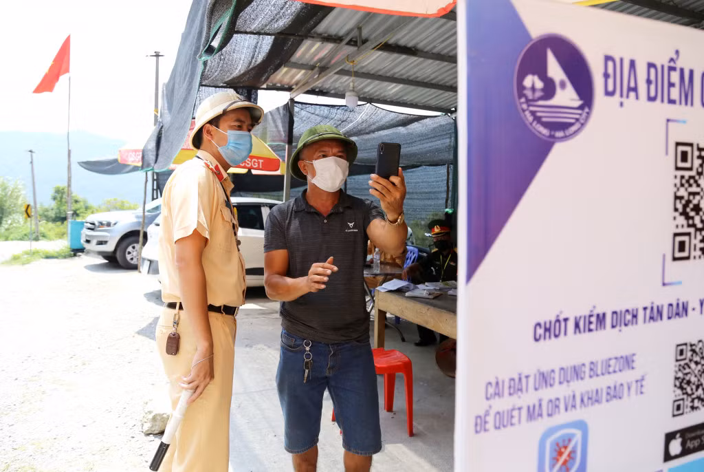 Cán bộ công an hướng dẫn người dân quét mã QRcode qua chốt kiểm soát dịch Covid-19 trên quốc lộ 279.