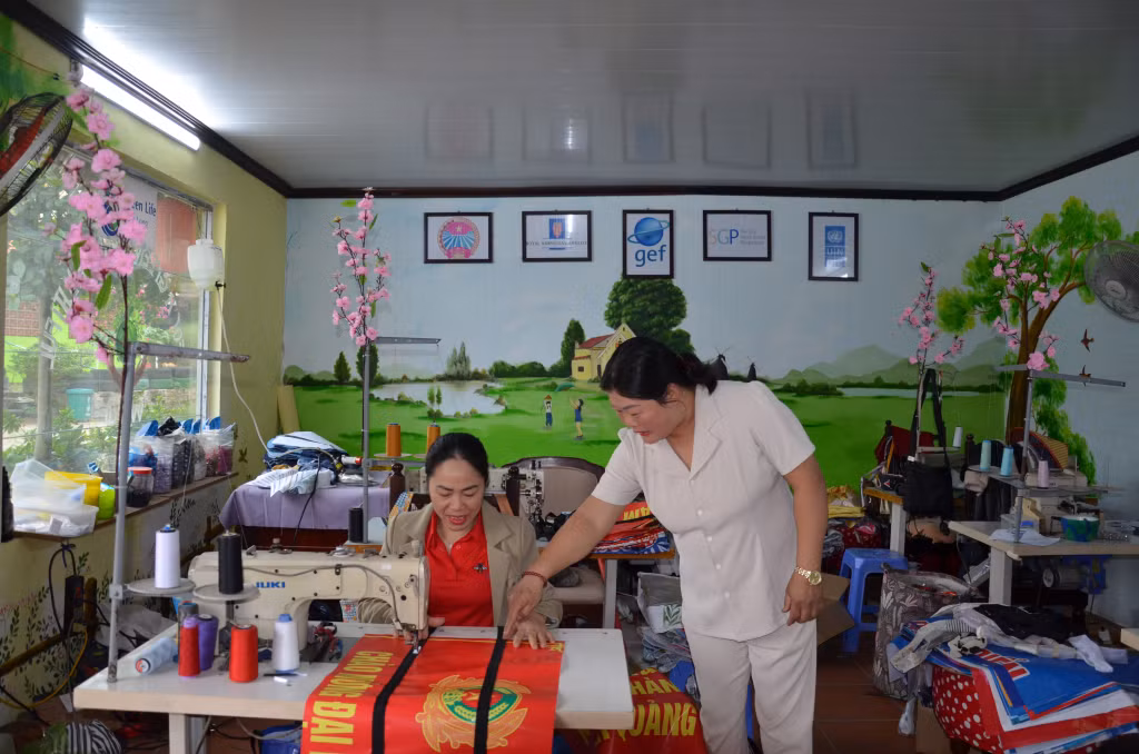 Chị Trần Thị Hương, Giám đốc HTX Sản xuất sản phẩm tái chế và dịch vụ tổng hợp Green Life Hạ Long (bên phải) (phường Hà Khẩu, TP Hạ Long) hướng dẫn nhân viên may túi đi chợ từ bạt của pano tuyên truyền cũ.