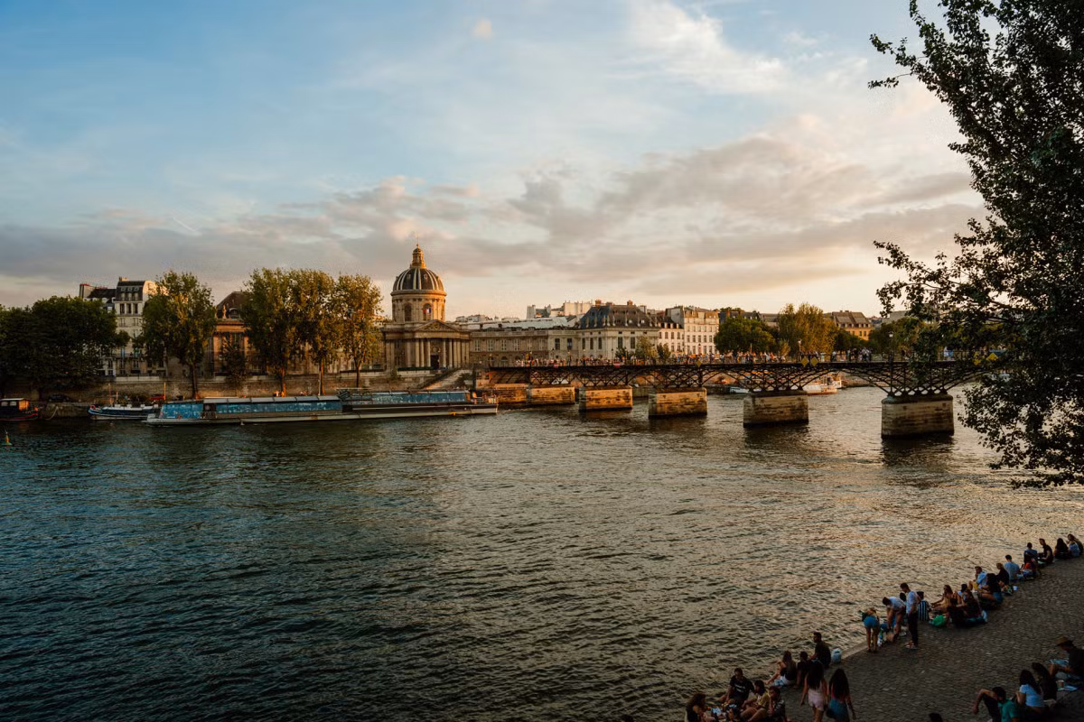 Phía xa là cầu Pont des Arts, bắc qua sông Seine. Trước đây, cầu còn được biết đến với tên gọi Cầu khóa tình yêu, do có hàng trăm nghìn ổ khóa được treo trên thành.