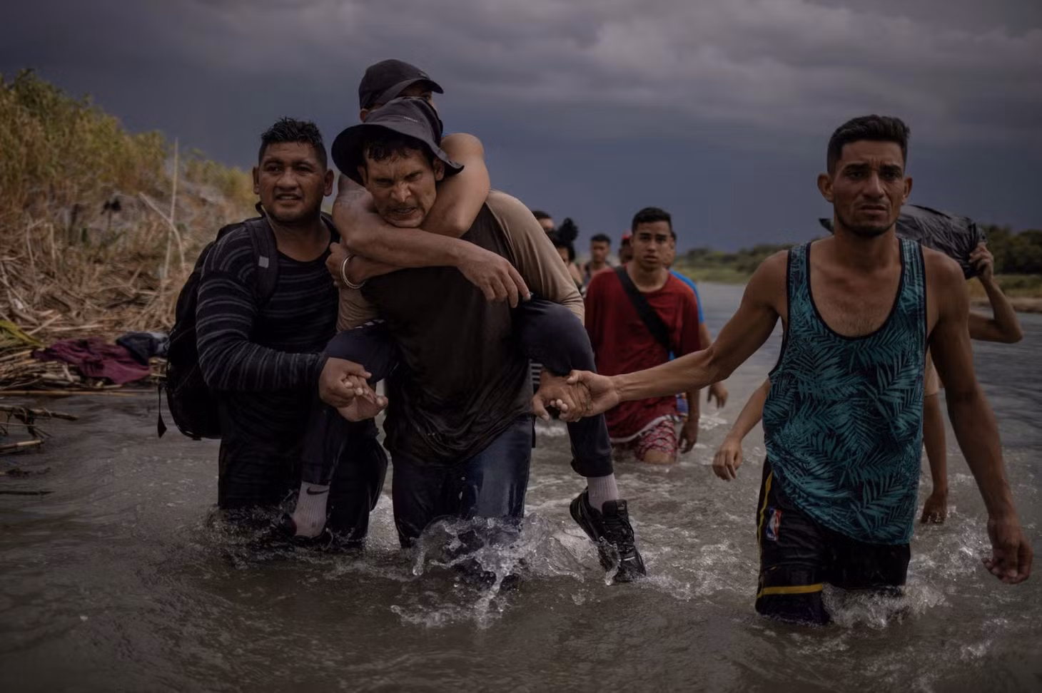 Một người đàn ông cõng người em họ bị tật nguyền lội qua sông Rio Grande, với sự giúp đỡ của 2 người đồng hương ngày 15/9/2023. Ảnh: Reuters