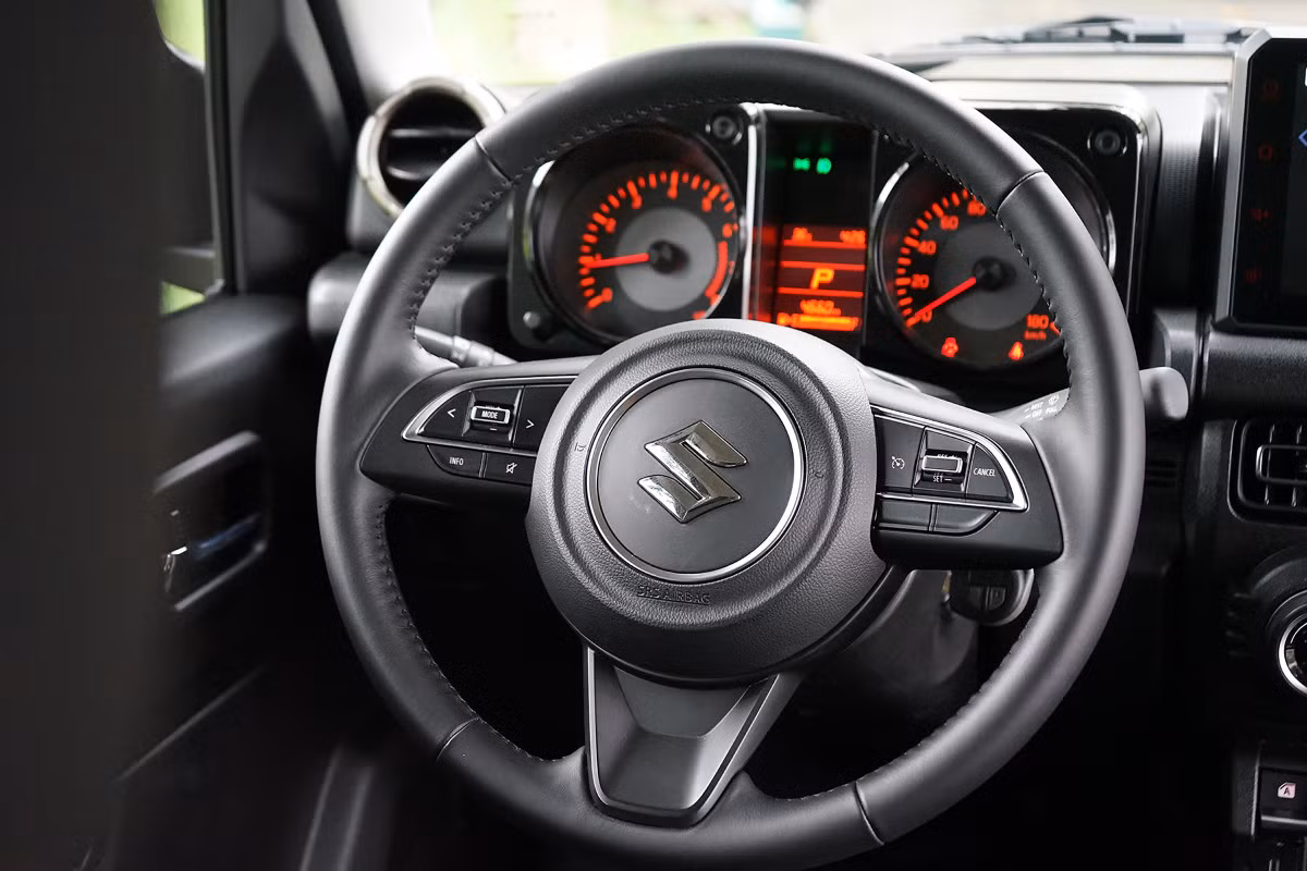 Vô-lăng ba chấu kèm một số phím chức năng cơ bản trên Jimny. Phía sau là đồng hồ tốc độ dạng analog kèm một màn hình LCD cỡ nhỏ ở giữa.
