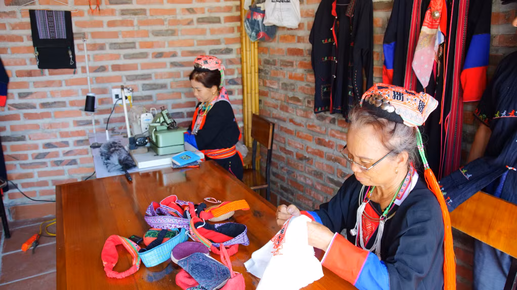 Phụ nữ Dao Thanh Y trình diễn nghệ thuật thêu truyền thống và bán các sản phẩm thủ công từ nghề thêu cho du khách tại Mô hình du lịch cộng đồng xóm Gốc Đa, thôn Khe Sú 2.