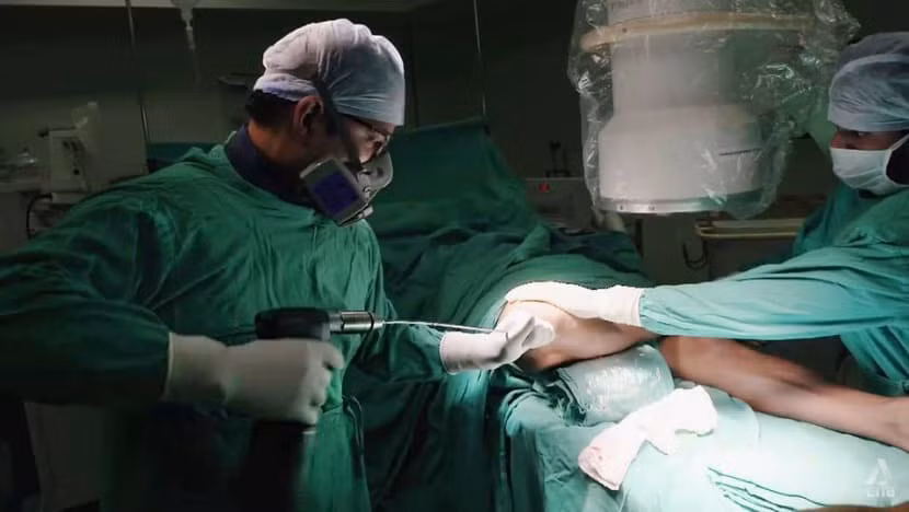 Bác sĩ phẫu thuật khoan dây và đinh vào chân của bệnh nhân. Ảnh: CNA