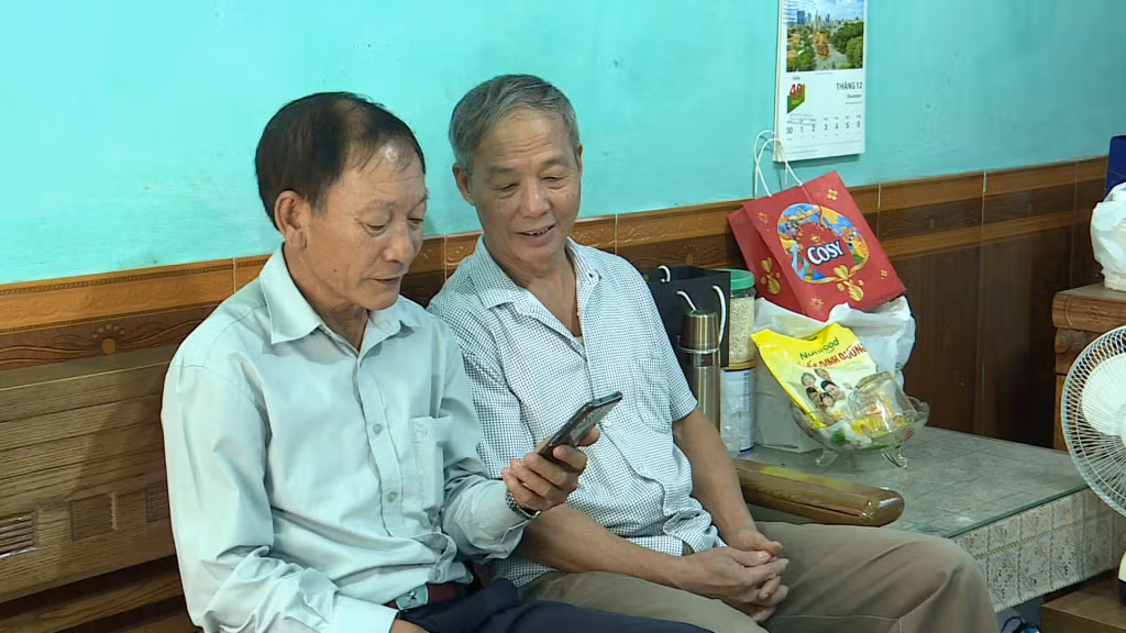 Ông Phạm Văn Biên (bên trái) hướng dẫn người dân tìm hiểu Luật Giao thông trên điện thoại.