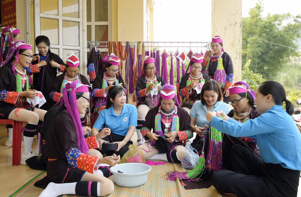 Các cán bộ mặt trận và các tổ chức chính trị xã hội xã Tiên Yên cùng phối hợp hỗ trợ, hướng dẫn các thế hệ trẻ ở thôn Nà Cà thêu hoa văn đồng bào dân tộc. 
