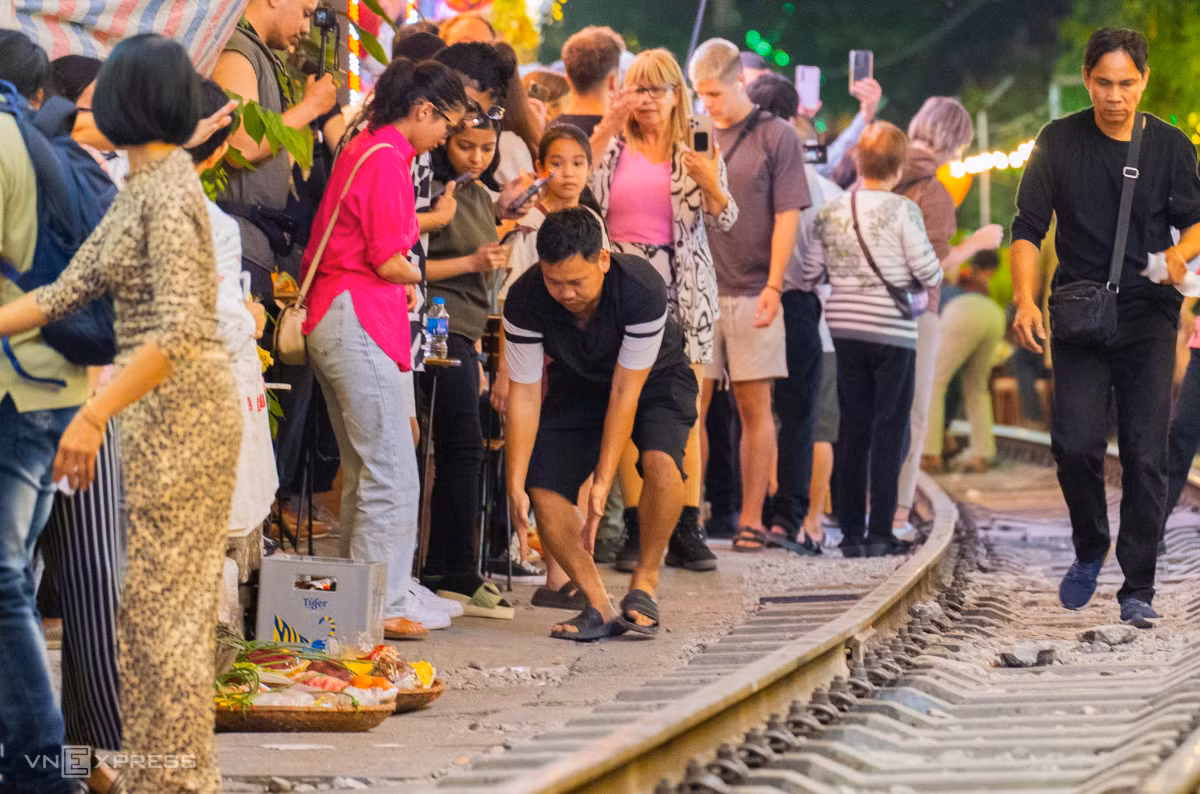 Khi chuông báo tàu qua vang lên, chủ cửa hàng chạy ra hướng dẫn du khách ngồi tránh vị trí tàu chạy. Nhiều người dùng loa, thổi còi để nhắc nhở du khách.