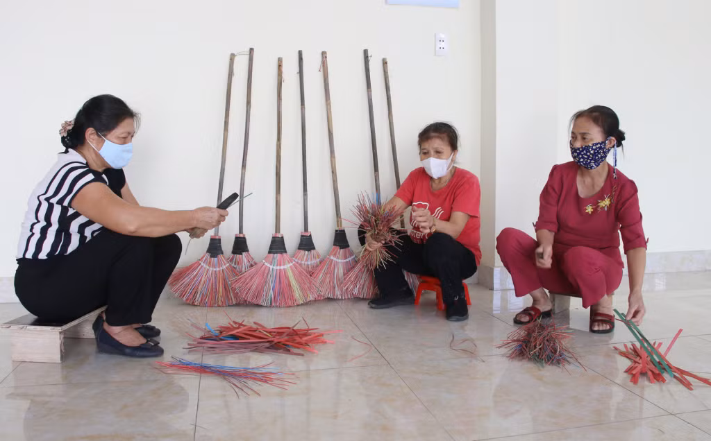 Bà Lê Thị Minh Huệ (bên trái) cùng thành viên Tổ đan chổi tái chế chẻ dây đan chổi.