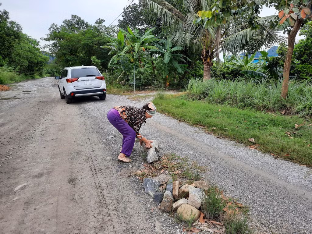 Bà Ng.Th.T (tổ 54, khu 6B) hì hụi vần những hòn đá rơi trên đường để đảm bảo ATGT.