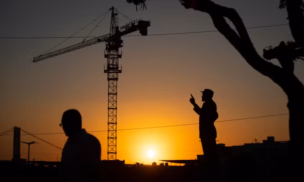 Một người đi bộ (bên trái) đi ngang qua cần cẩu xây dựng và tượng đài Samora Machel, vị Tổng thống đầu tiên của Mozambique (bên phải), trong ánh hoàng hôn tại thủ đô Maputo, Mozambique, ngày 3/9/2019. Ảnh: AP