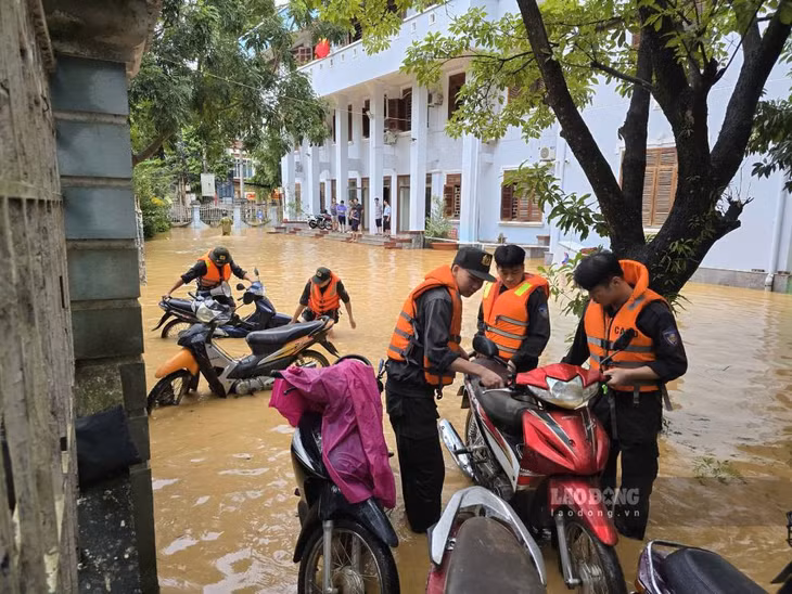 Lực lượng chức năng hỗ trợ di dời xe máy của người dân đến khu vực cao khi mực nước lũ dâng. Ảnh: Tân Văn.