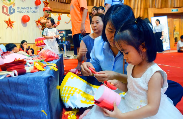 Một bé chăm chú tự tay hoàn thành chiếc đèn lồng mới từ giấy màu.