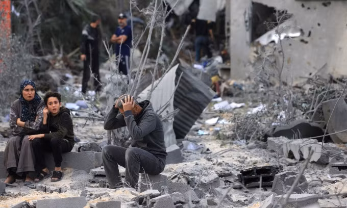 Người dân ngồi giữa đống đổ nát của ngôi nhà bị Israel tập kích ở Khan Yunis, phía nam Dải Gaza, hôm 22/11. Ảnh: AFP