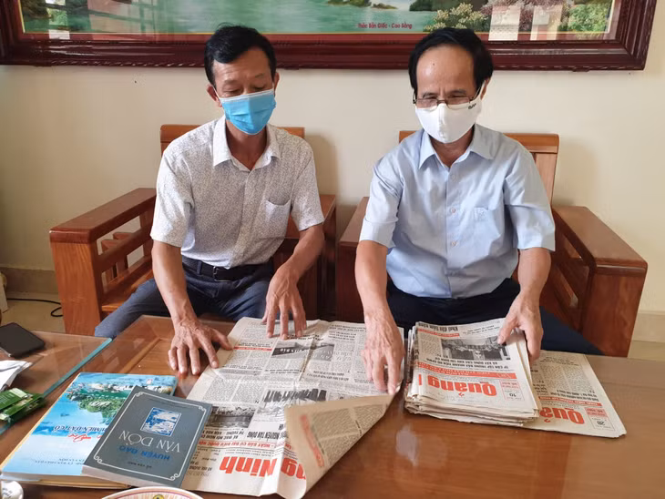 ông Nguyễn Minh Trang (bên phải) lật giở lại những bài báo khi xưa viết về Vân Đồn