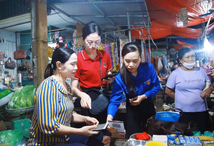Đoàn thanh niên và nhân viên ngân hàng hướng dẫn các tiểu thương kinh doanh tại chợ Tiên Yên thực hiện việc thanh toán không dùng tiền mặt trong kinh doanh.